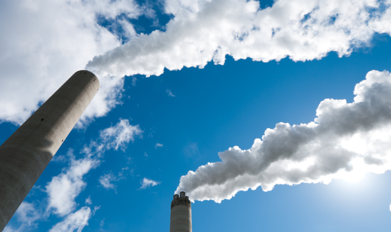 Two industrial smoke stacks emitting white clouds of smoke against a blue sky