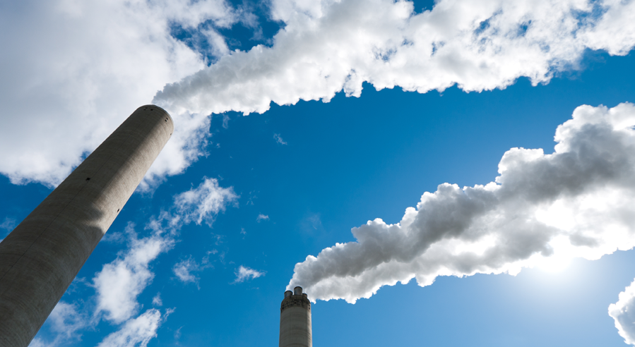 Two industrial smoke stacks emitting white clouds of smoke against a blue sky