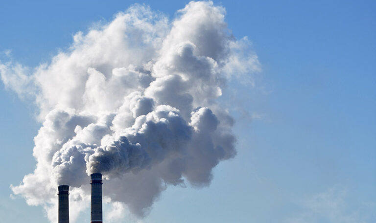 Two industrial smoke stacks emitting white clouds of smoke against a blue sky