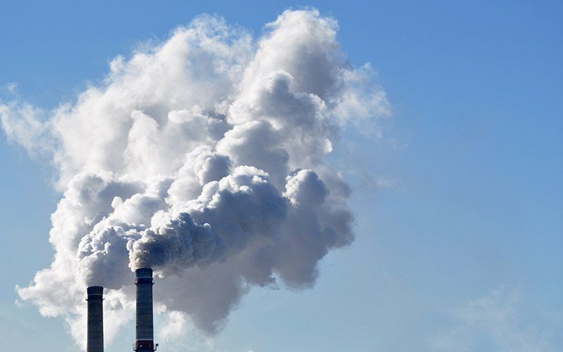 Two industrial smoke stacks emitting white clouds of smoke against a blue sky